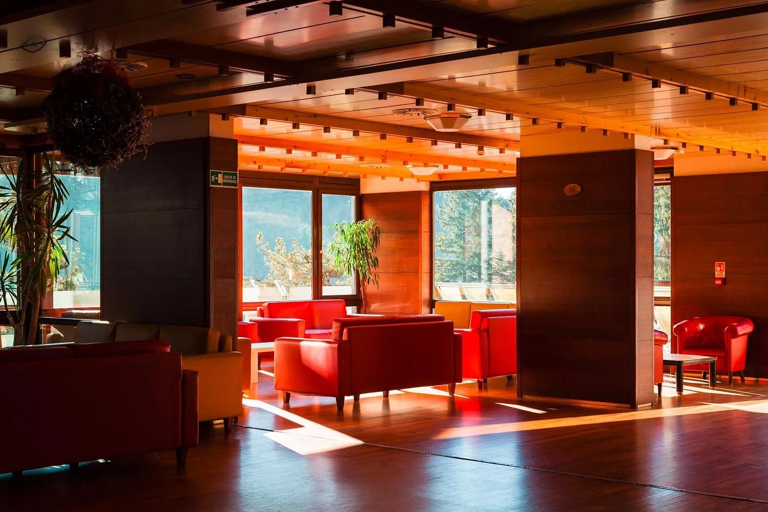 Area lounge con poltrone in pelle rossa, soffitto in legno e ampie vetrate illuminate dal sole
