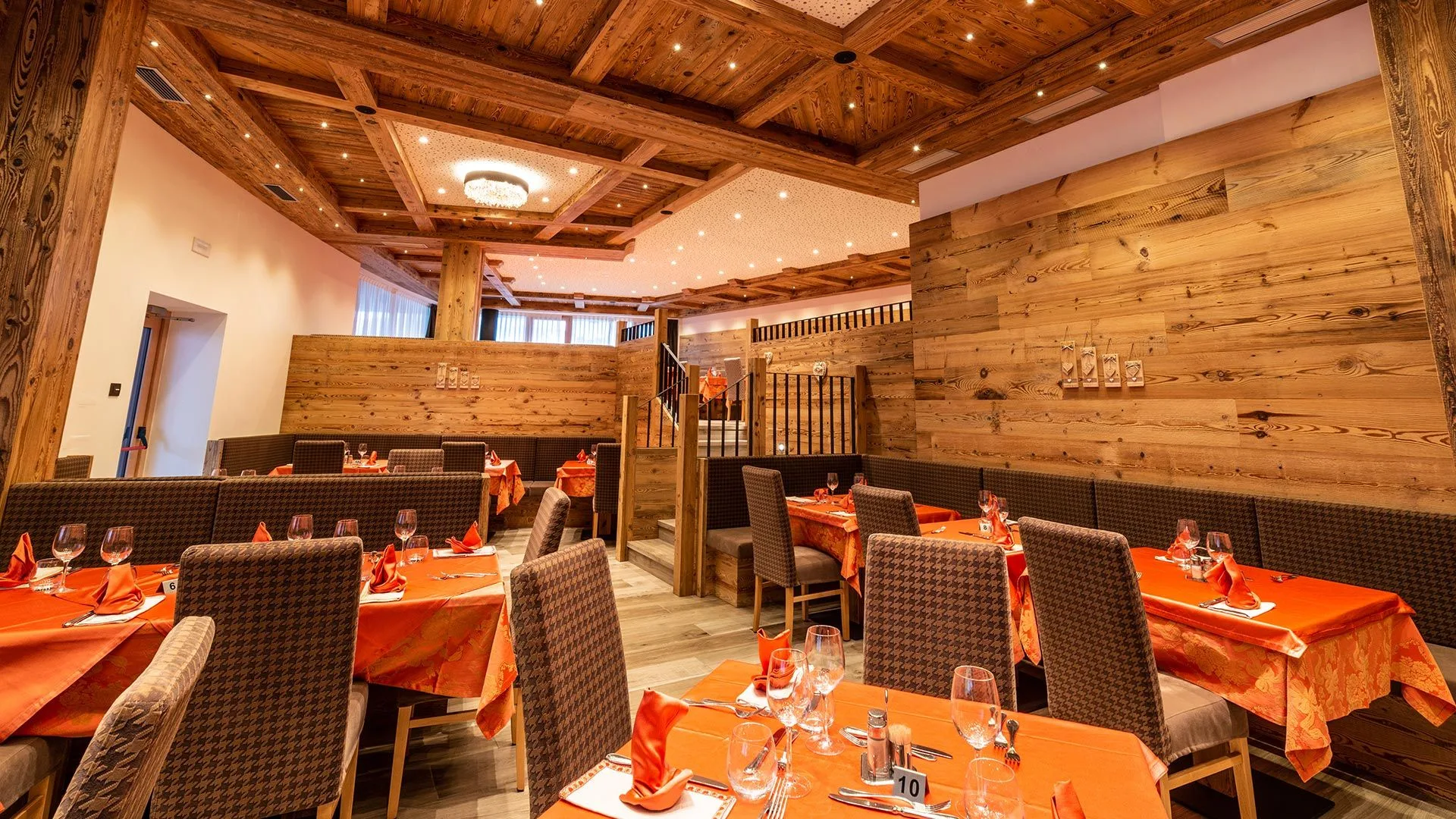 Sala ristorante con pareti in legno, tovaglie arancioni e soffitto a cassettoni