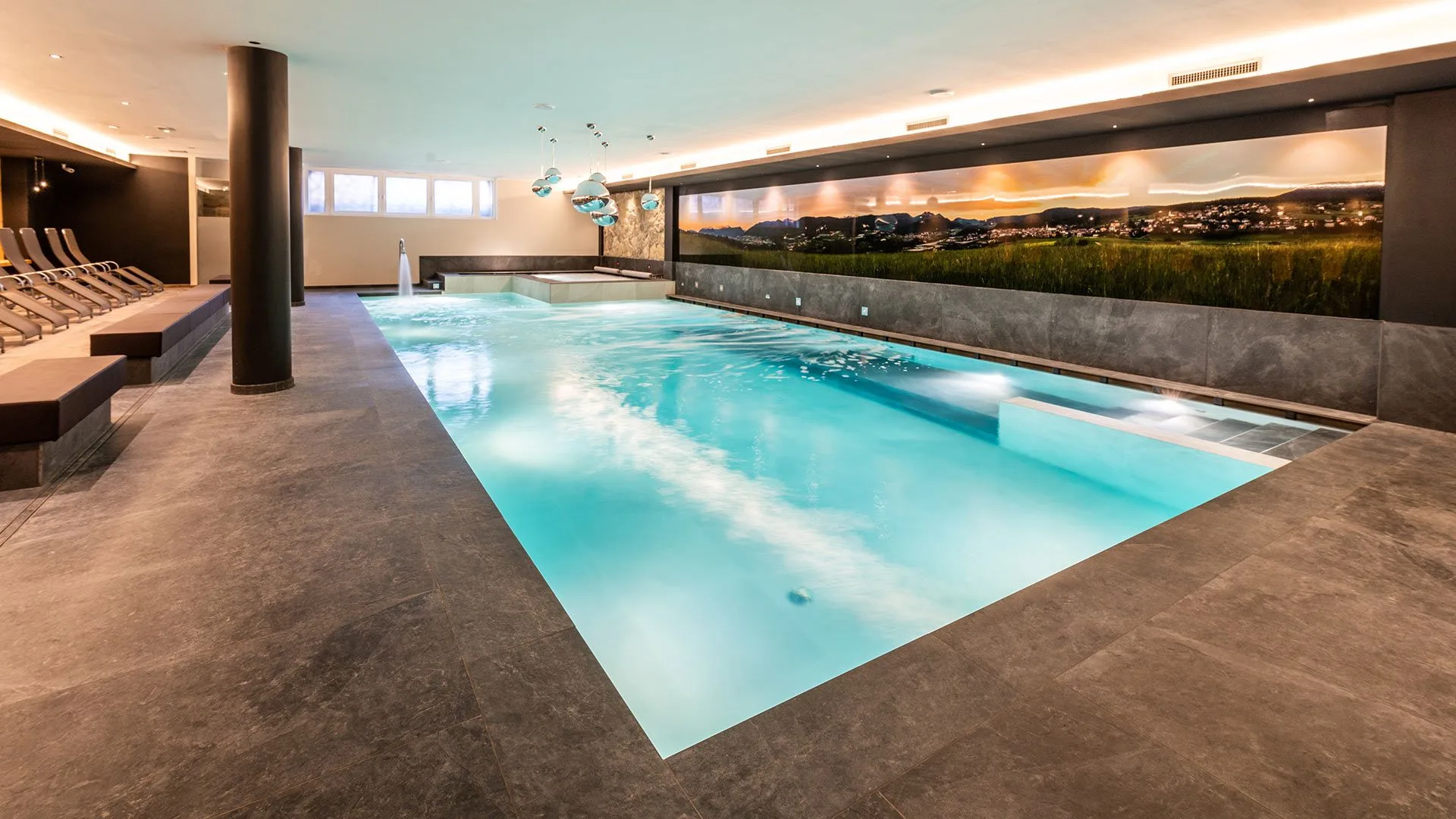 Piscina coperta con acqua turchese, cascata e vista su murale alpino