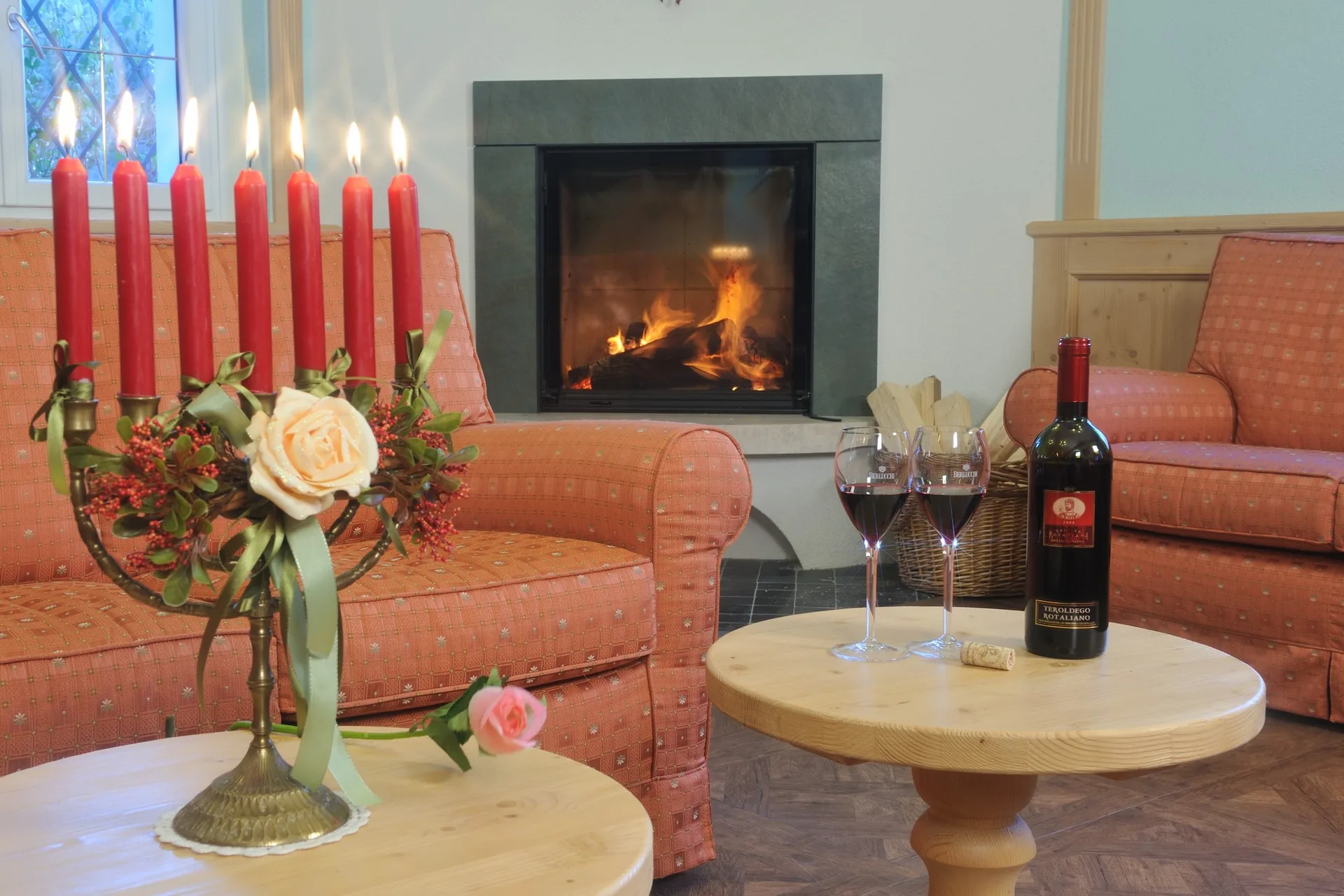 Angolo relax con camino acceso, poltrone, candele rosse e bottiglia di vino