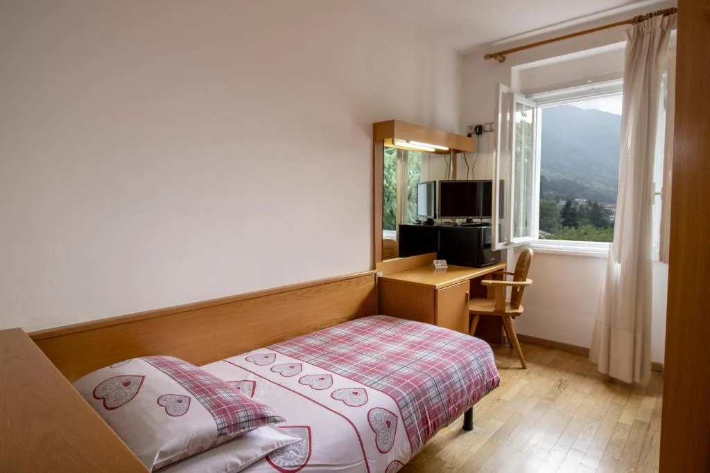 Camera singola con letto, scrivania e finestra con vista sulle montagne