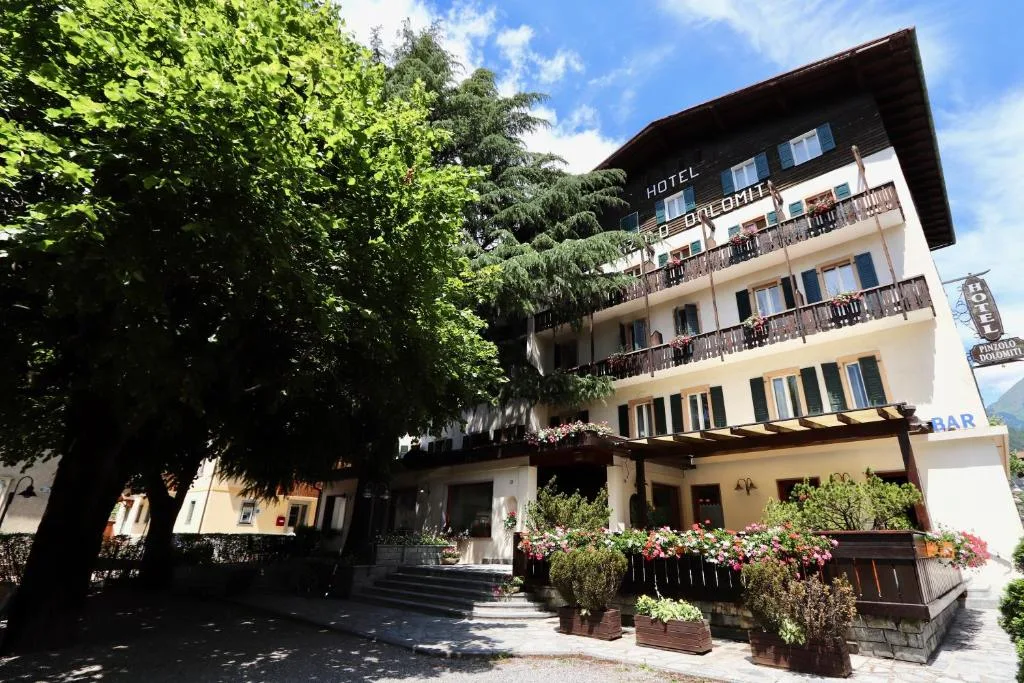 Facciata dell'hotel di giorno con alberi, balconi fioriti e insegna
