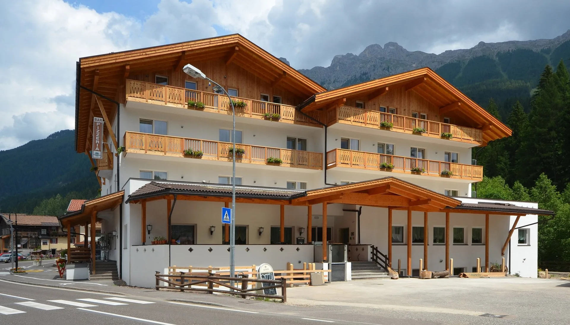Facciata dell'hotel in estate con balconi fioriti e montagne sullo sfondo