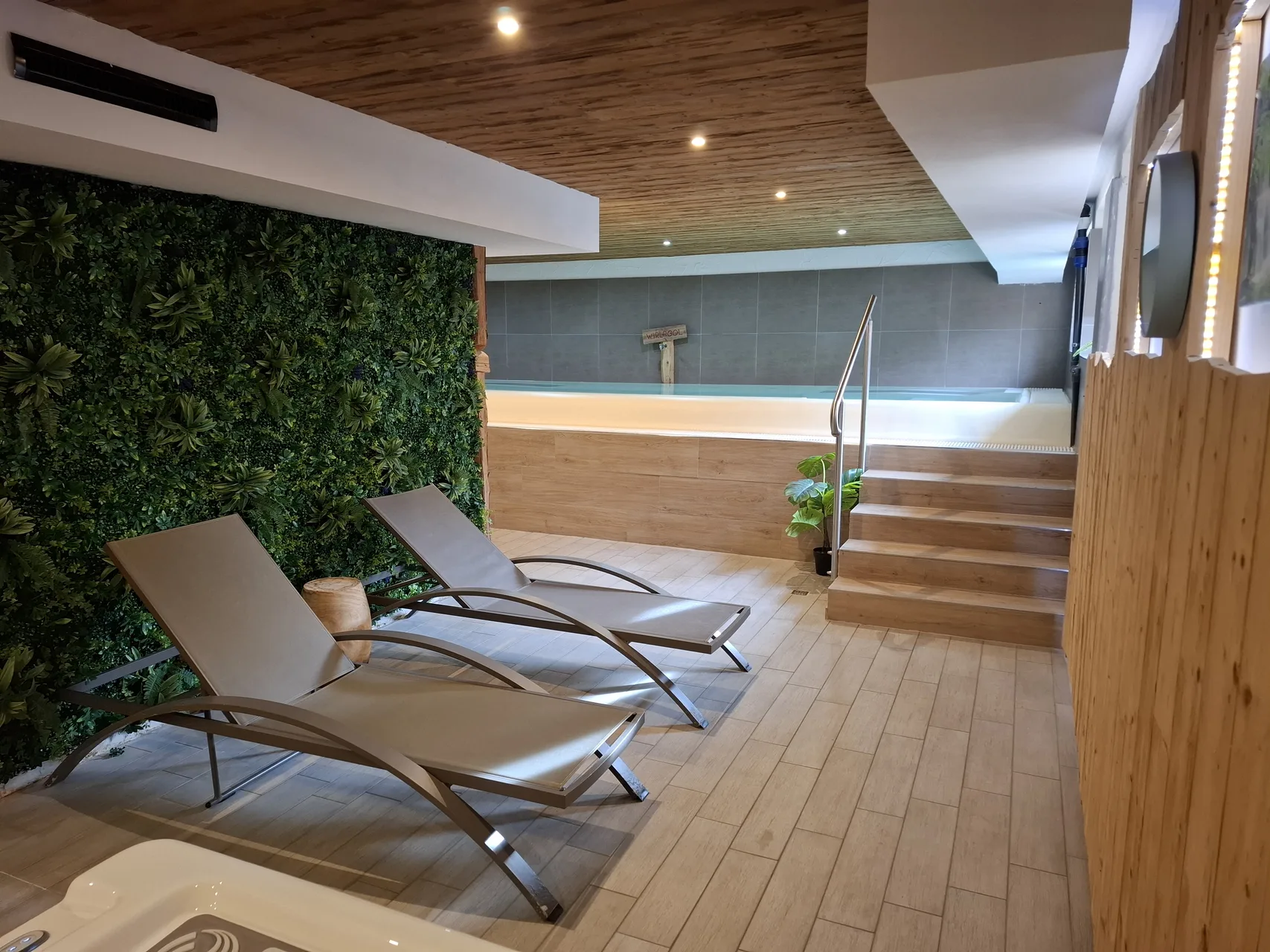 Zona relax spa con lettini prendisole e parete di verde vicino alla piscina