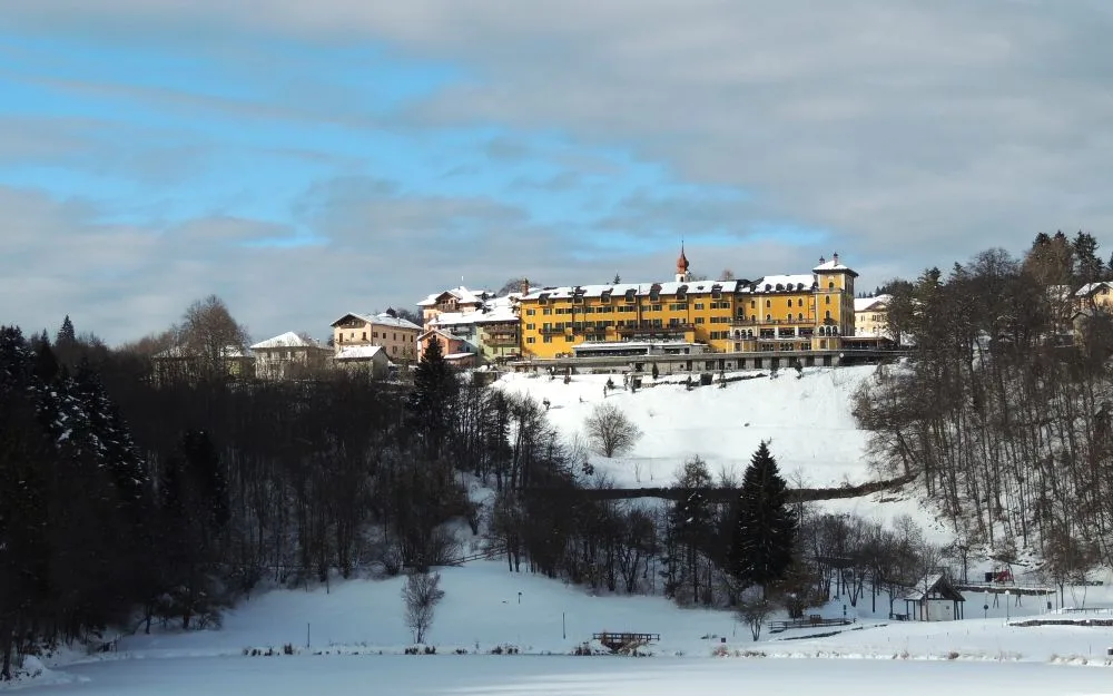 Hotel giallo su collina innevata circondato dal bosco in inverno