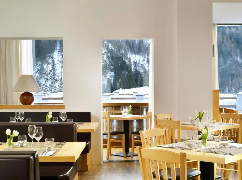 Sala ristorante luminosa con tavoli apparecchiati e vista sui boschi innevati