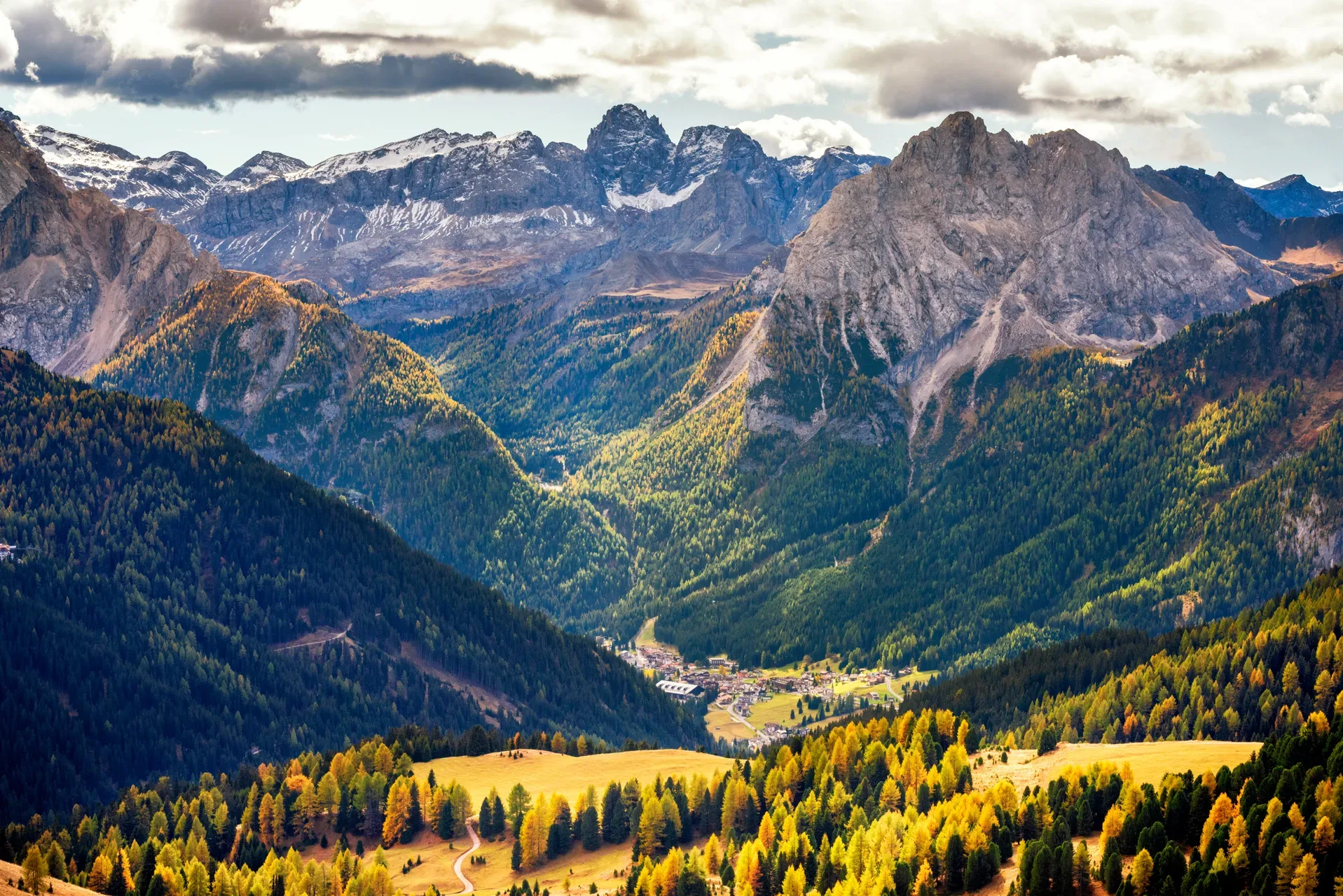 Panorama autunnale sulla valle con borgo, boschi dorati e vette dolomitiche