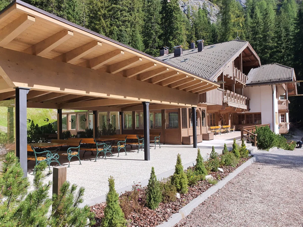 Portico coperto in legno con panche e tavoli accanto all'edificio dell'hotel circondato da abeti