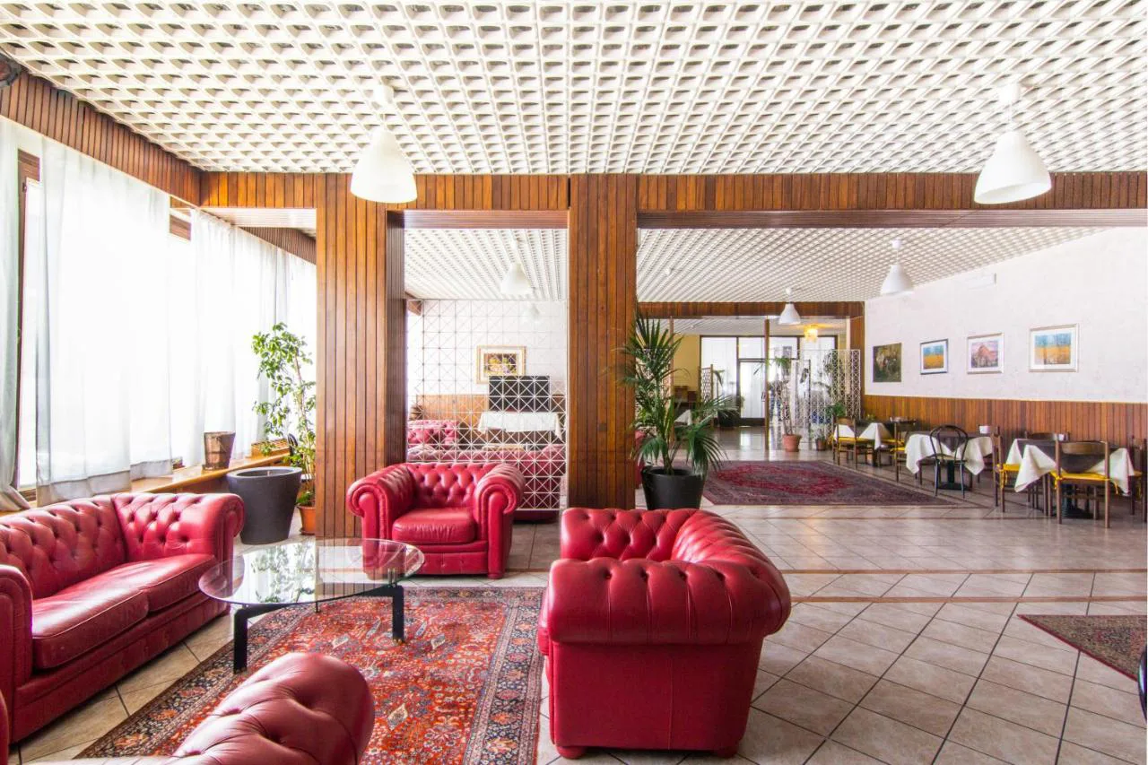 Zona lounge con divani in pelle rossa, piante e vista sulla sala ristorante