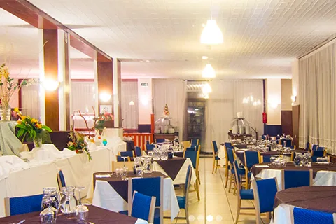 Sala ristorante con tavoli apparecchiati e sedie blu illuminata