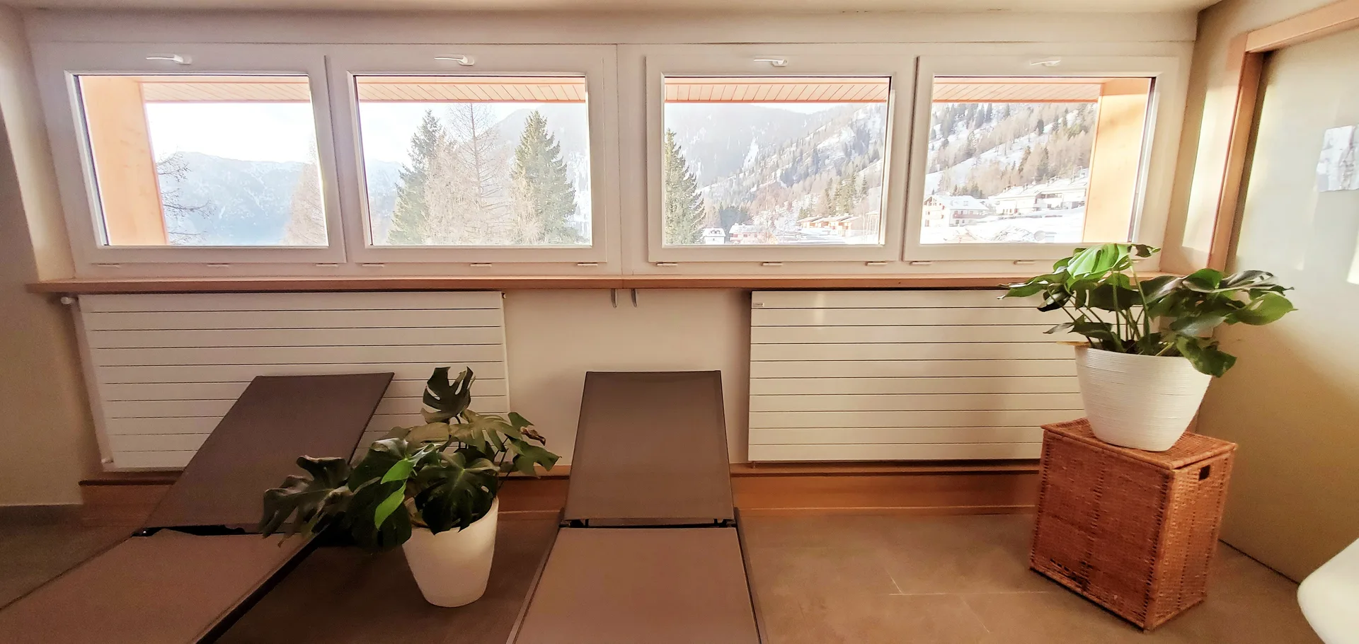 Area relax con lettini, piante verdi e grandi finestre con vista sulle montagne innevate