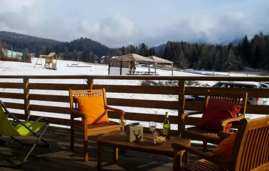 Terrazza con poltrone in legno e cuscini colorati affacciata su paesaggio innevato e parco giochi