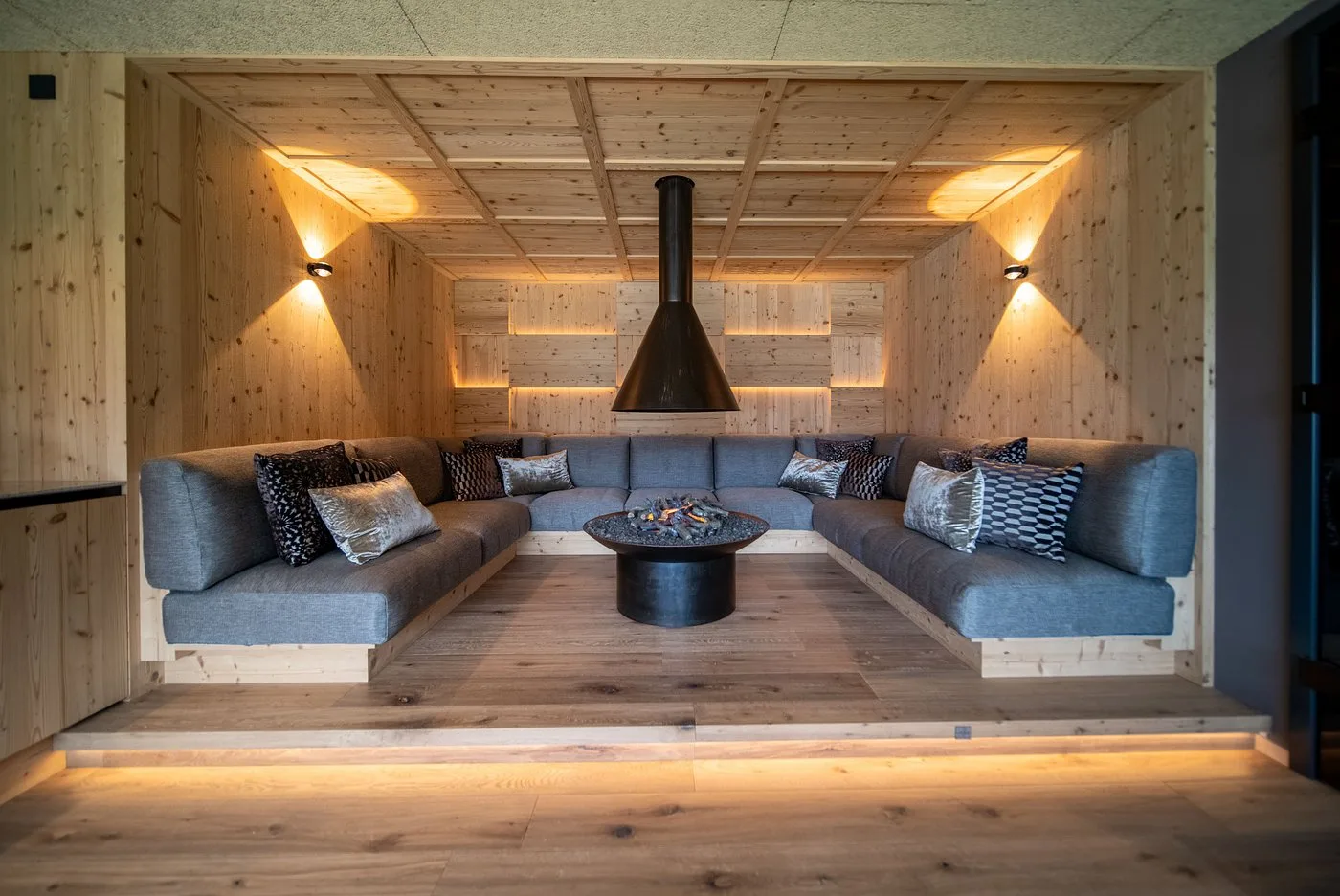 Sala relax in legno con divano angolare grigio e camino sospeso