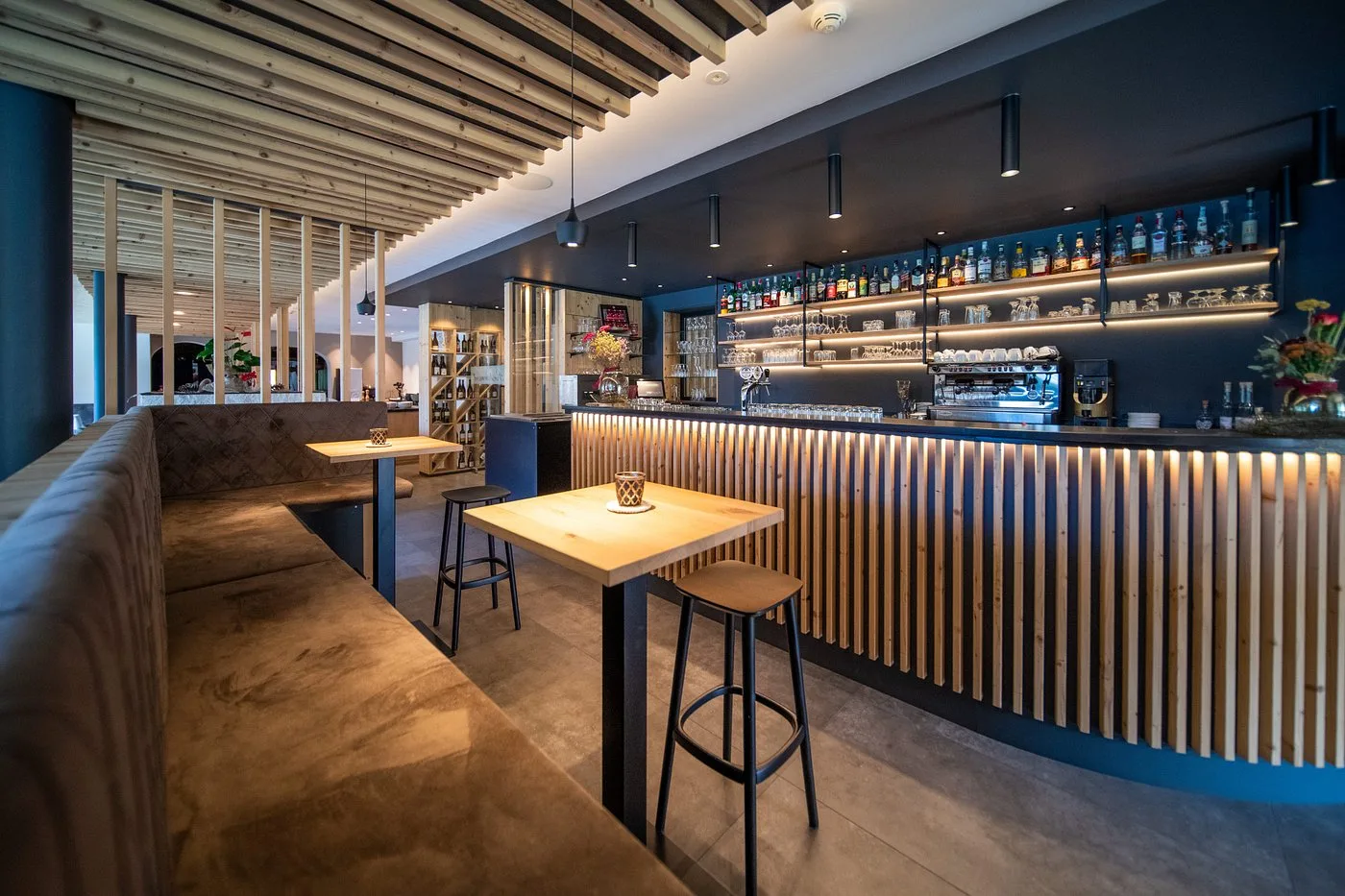 Bar dell'hotel con bancone illuminato in legno e tavoli alti