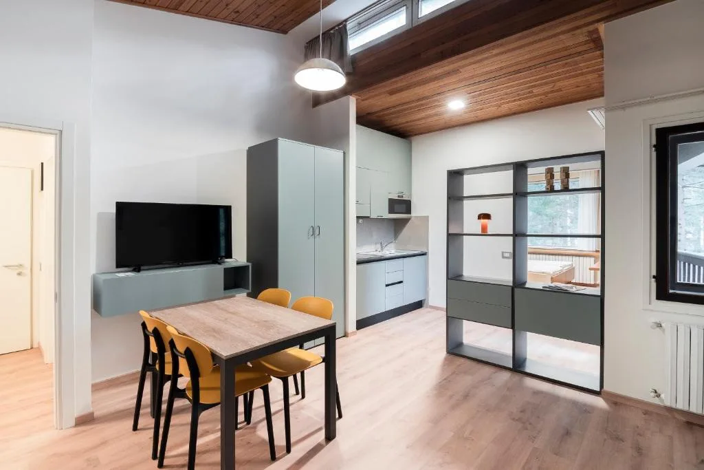 Zona living con angolo cottura, tavolo da pranzo e sedie gialle sotto soffitto in legno