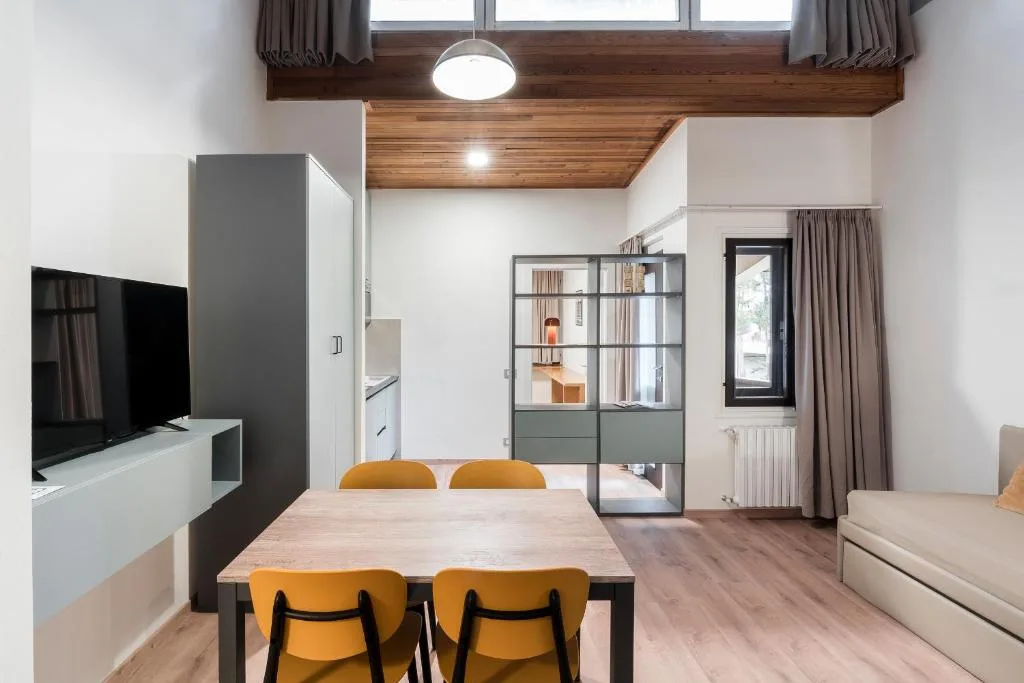 Soggiorno moderno con tavolo da pranzo, sedie gialle, TV e soffitto con travi in legno