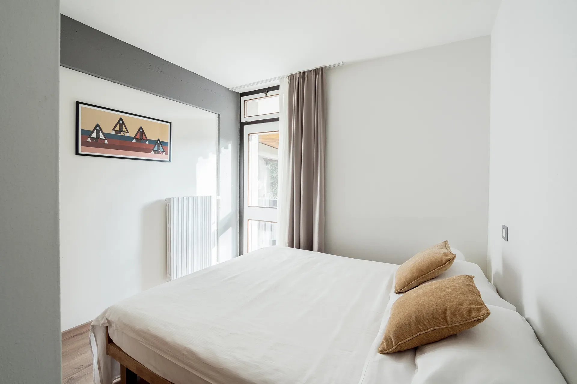 Camera da letto luminosa con letto matrimoniale, cuscini beige e quadro decorativo