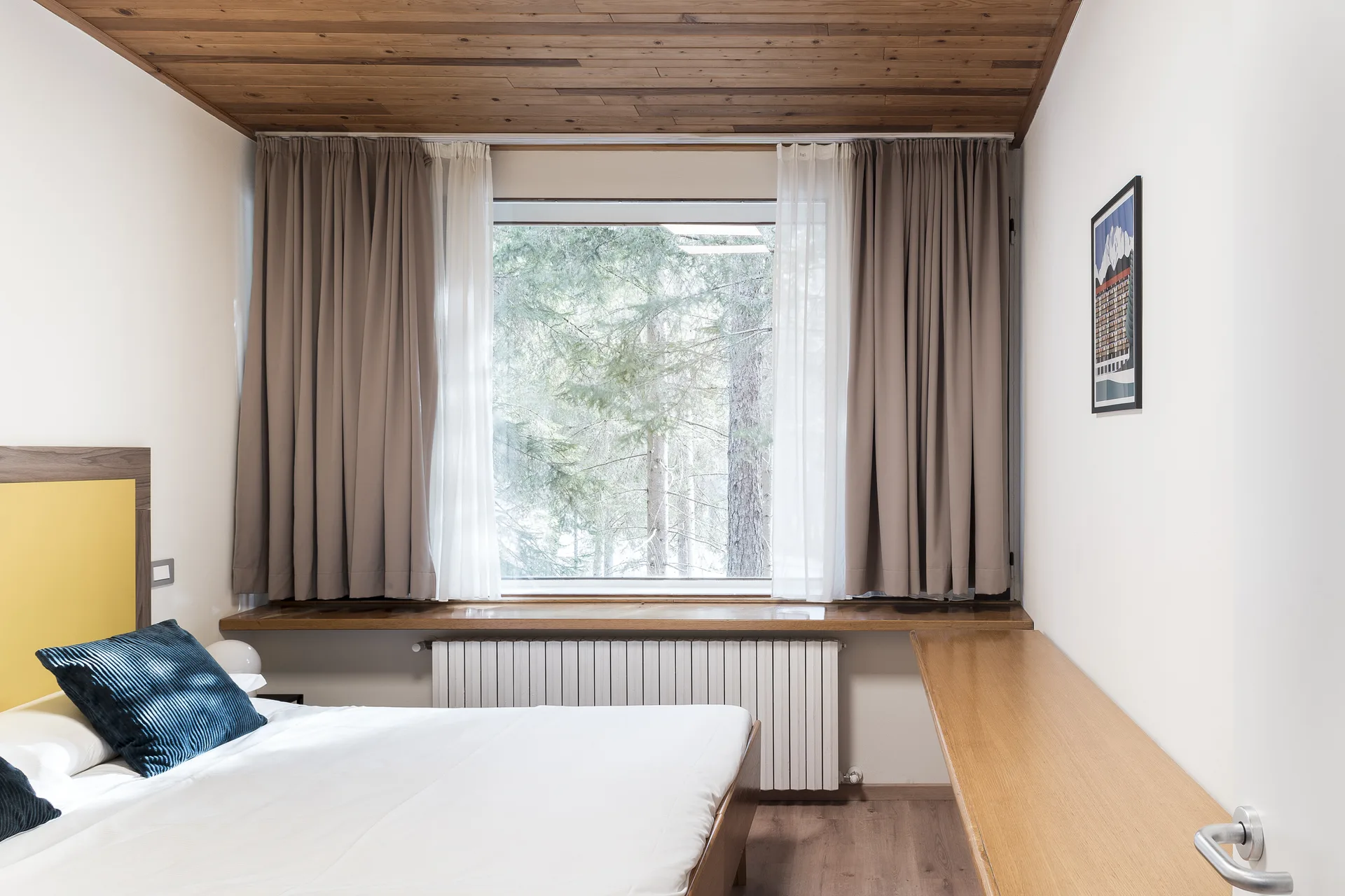 Camera da letto con soffitto in legno, finestra affacciata sul bosco e scrittoio