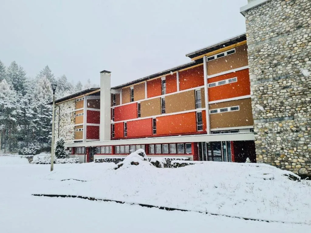 Esterno dell'hotel di montagna innevato con facciata colorata e alberi coperti di neve