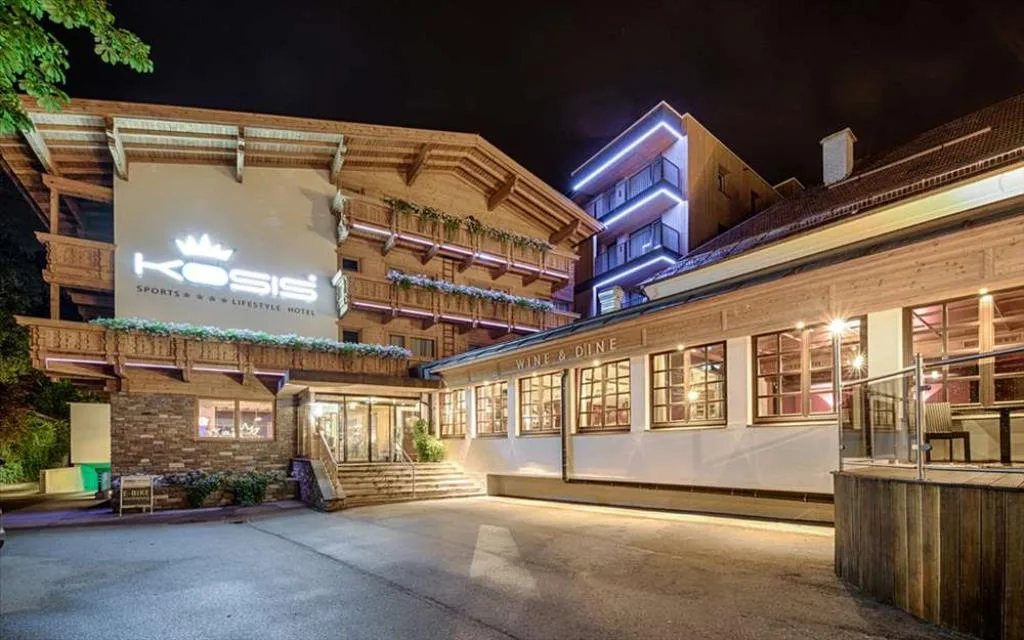 Facciata dell'hotel Kosis illuminata di sera con insegna e ristorante Wine & Dine