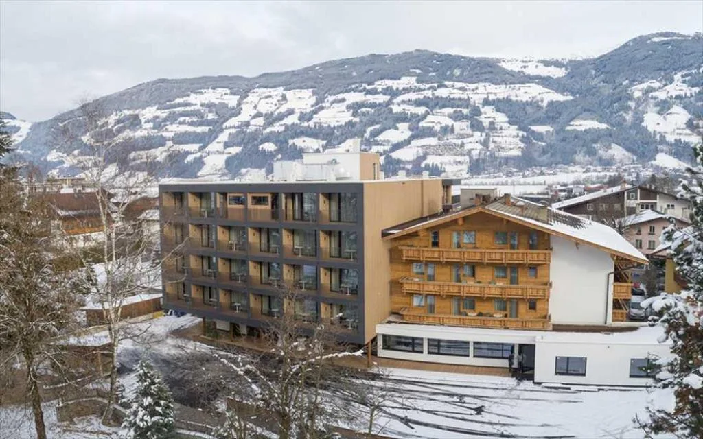 Esterno dell'hotel con edificio moderno e chalet in legno sullo sfondo delle montagne innevate
