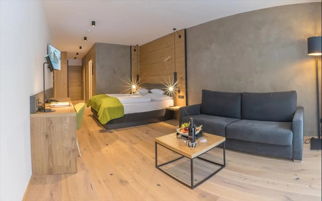 Ampia junior suite con letto, divano grigio e pavimento in legno