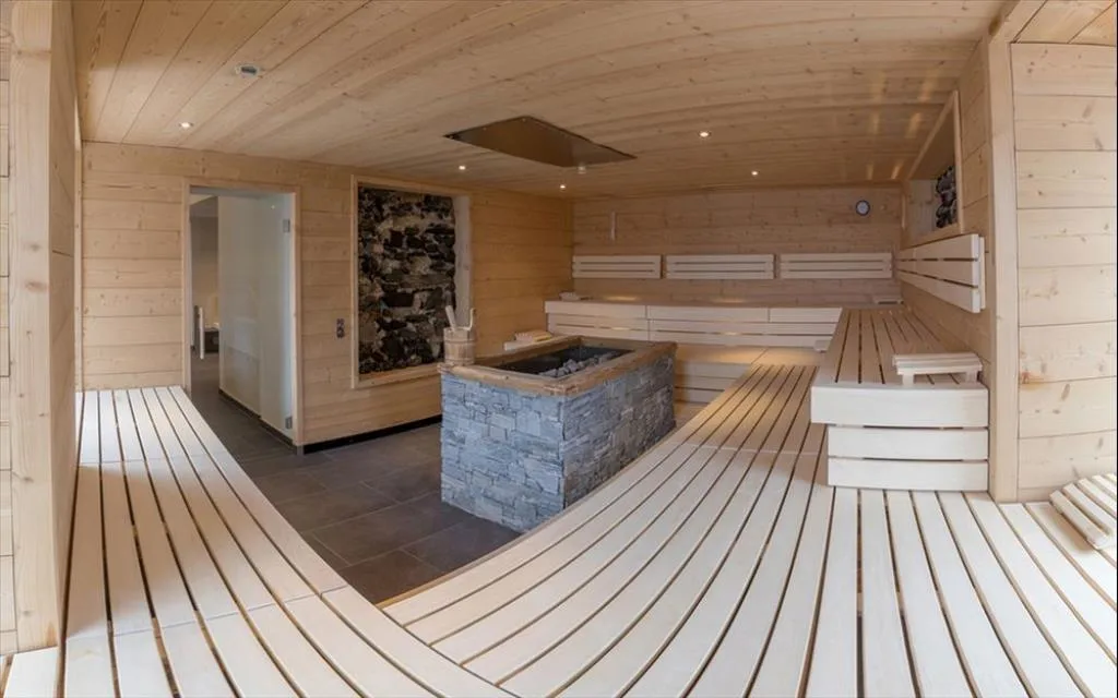 Ampia sauna in legno con stufa in pietra e panche disposte a semicerchio