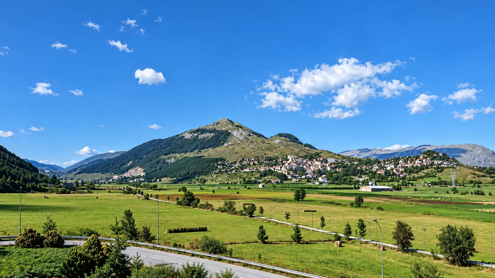 Panorama estivo di montagna con borgo sul pendio e prati verdi