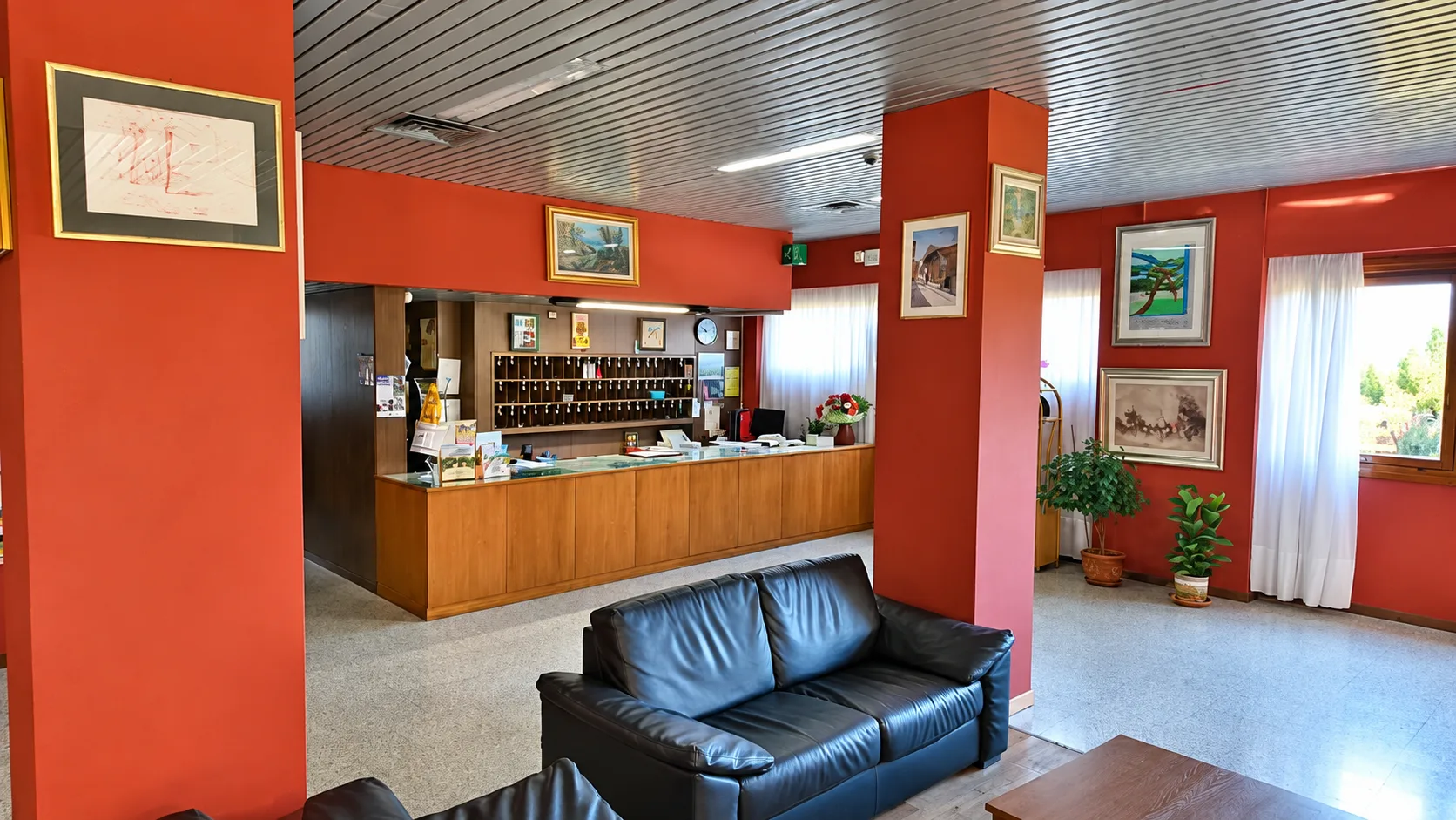 Hall dell'hotel con pareti rosse, reception in legno e divano in pelle nera