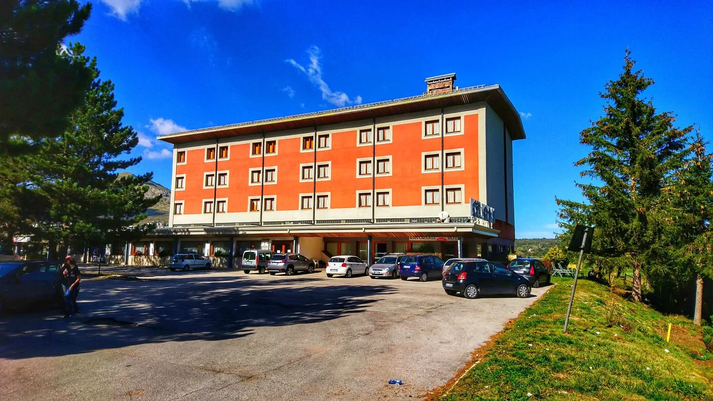 Facciata arancione dell'hotel con parcheggio e cielo azzurro in estate