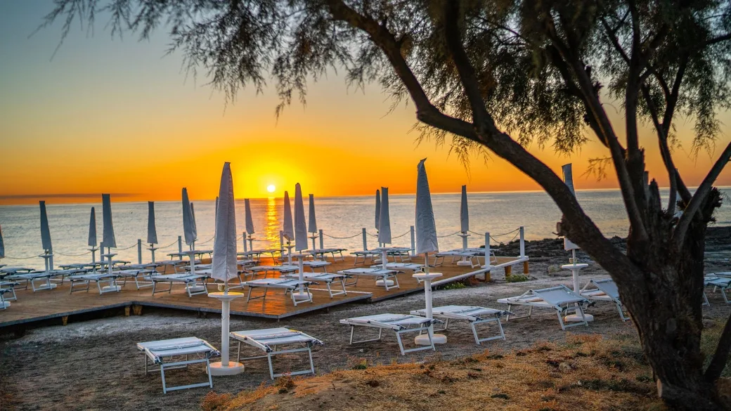 Solarium sulla scogliera al tramonto con lettini, ombrelloni e albero in primo piano