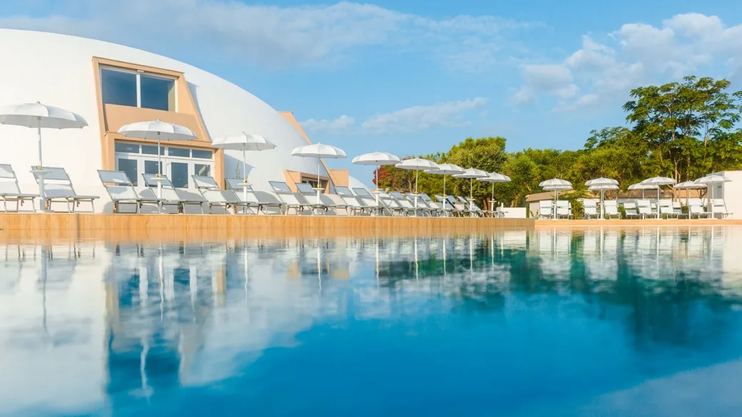 Piscina con lettini e ombrelloni davanti all'edificio a cupola del resort