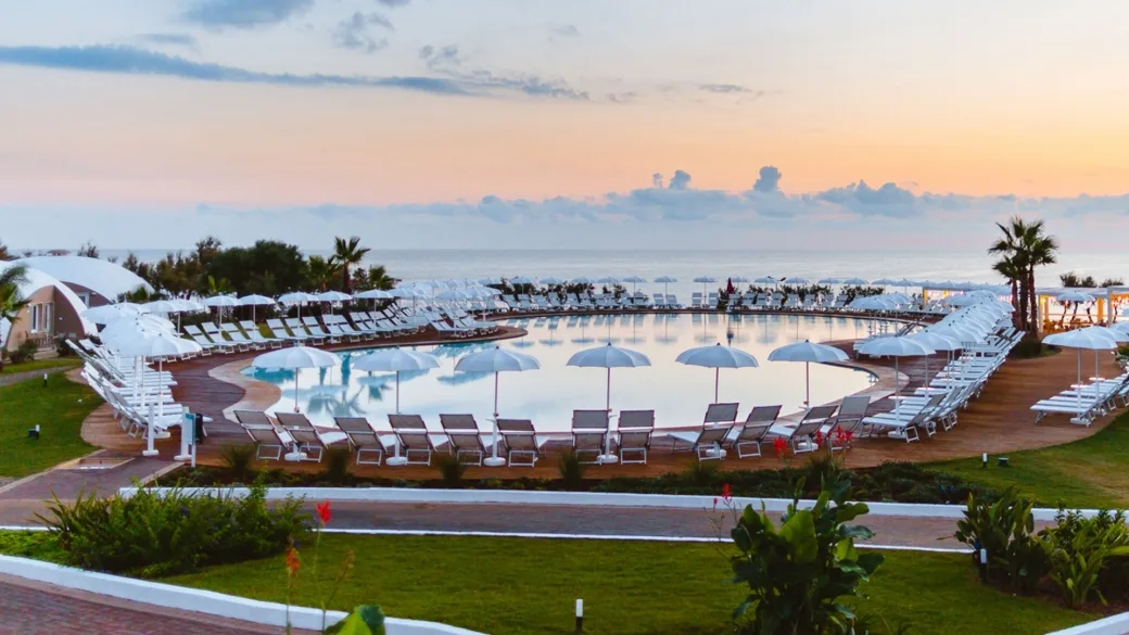 Veduta panoramica della piscina circolare con lettini e ombrelloni al tramonto sul mare