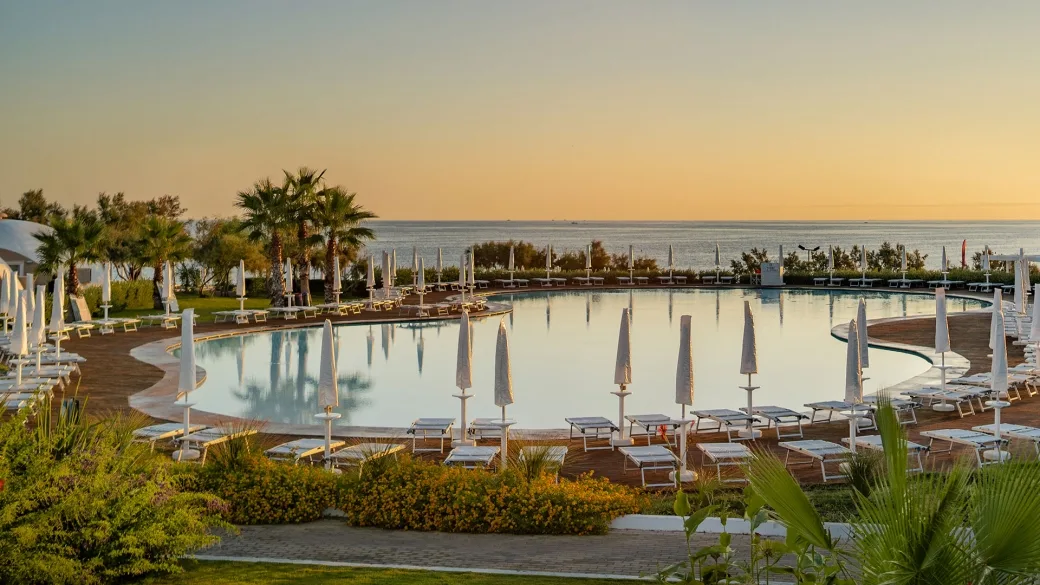 Piscina circolare con ombrelloni e lettini al tramonto immersa nel verde vista mare