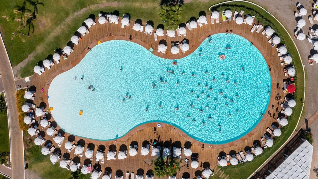 Vista aerea della piscina sagomata circondata da lettini e ombrelloni bianchi