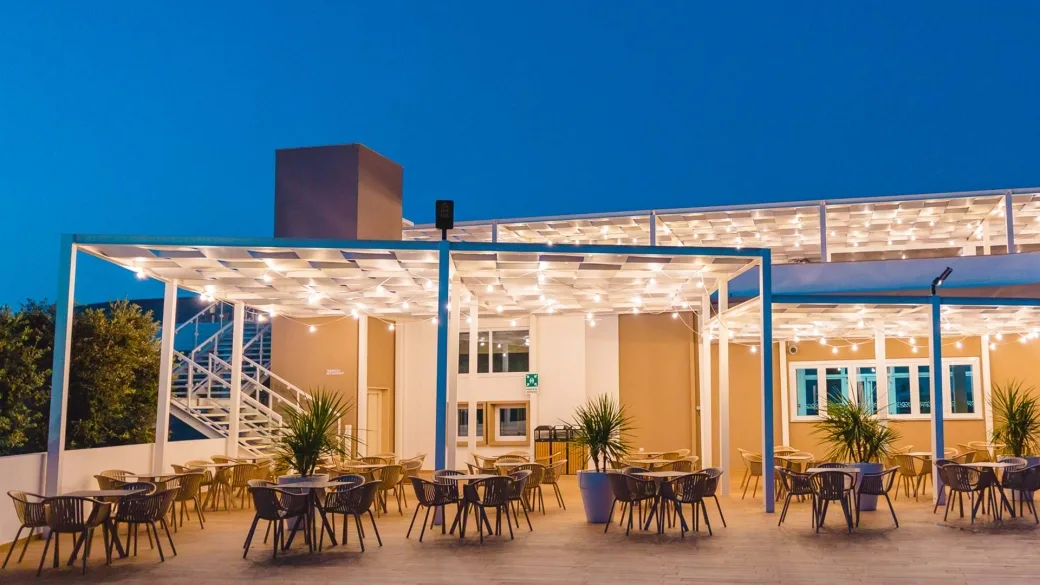 Terrazza esterna con tavoli, sedie e pergolato illuminato di sera