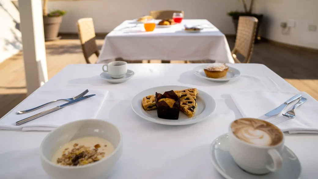 Dettaglio di colazione con cappuccino, dolci e cereali su tavolo in terrazza