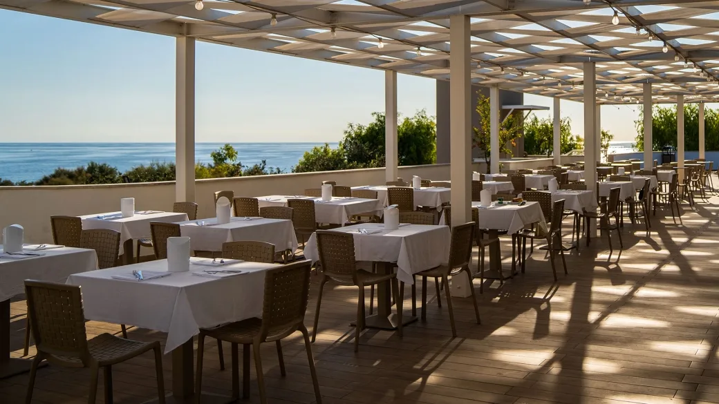 Terrazza ristorante con tavoli apparecchiati e pergolato affacciata sul mare