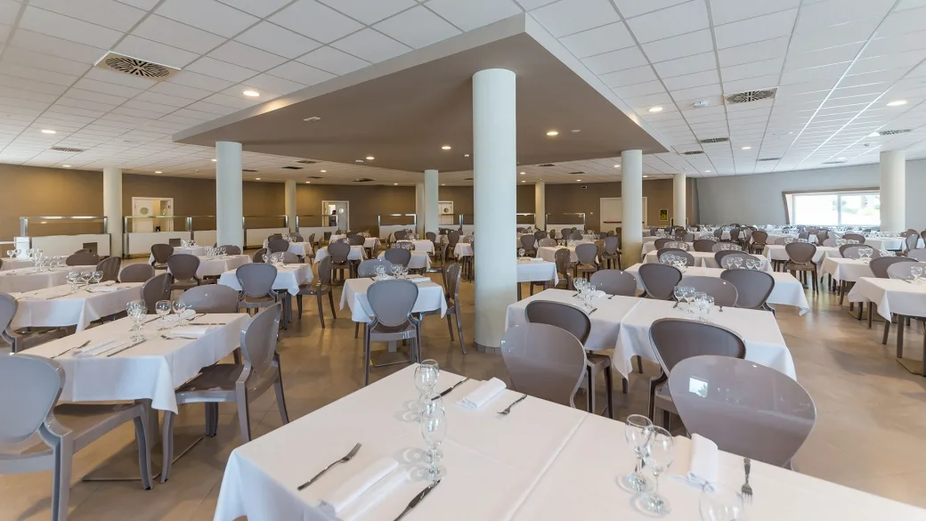 Sala ristorante interna con numerosi tavoli apparecchiati e bicchieri