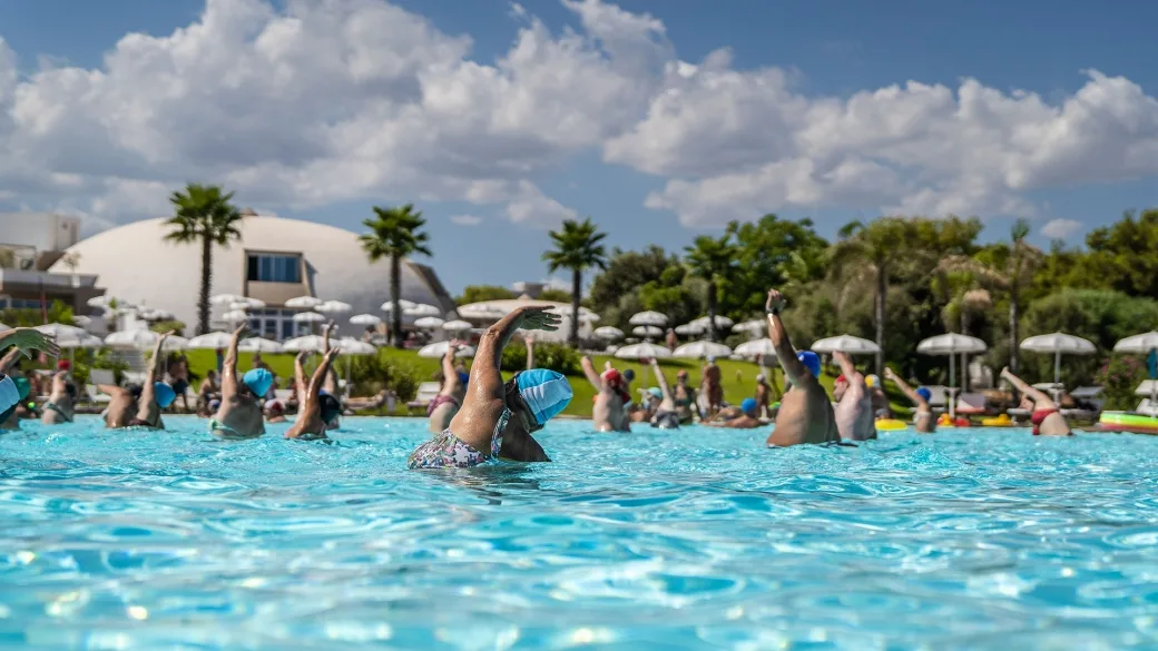 Lezione di acquagym in piscina con ospiti e vista sulla struttura del resort
