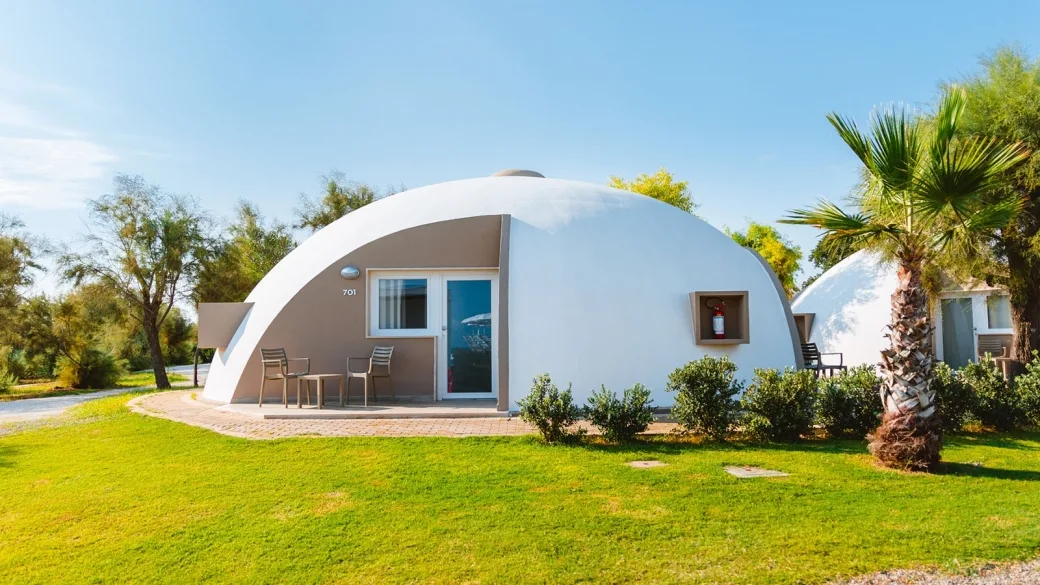 Bungalow a cupola bianco con terrazza, tavolino e sedie circondato dal prato