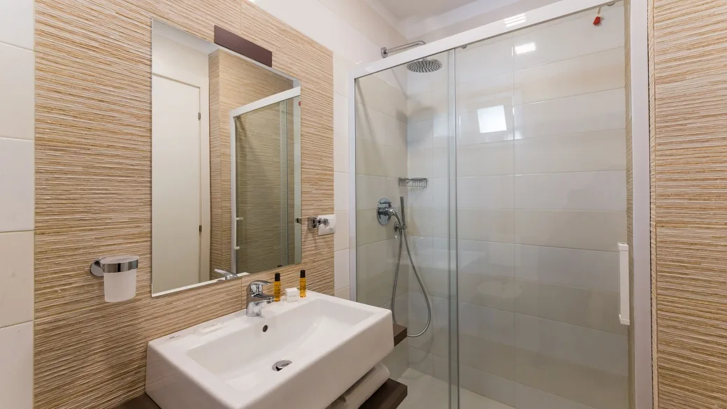 Bagno della camera con doccia, lavabo e specchio in toni chiari