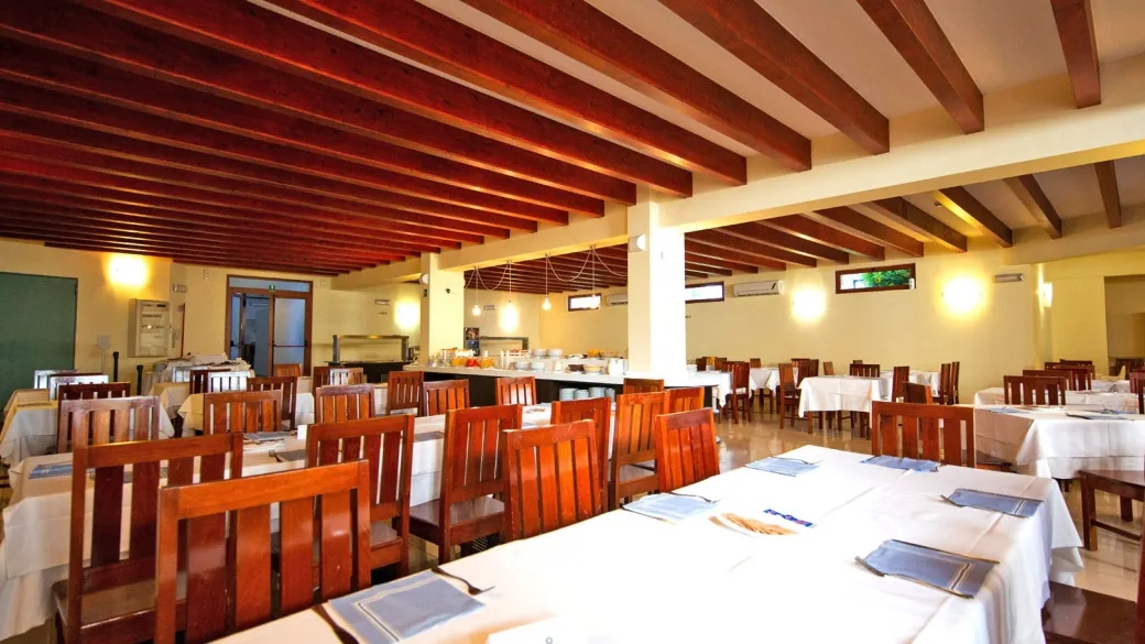 Sala ristorante interna con tavoli apparecchiati, sedie in legno e travi a vista sul soffitto