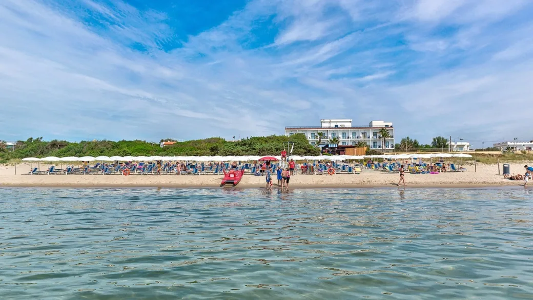 Vista dal mare dell'hotel fronte spiaggia con lettini, ombrelloni e bagnanti sulla sabbia