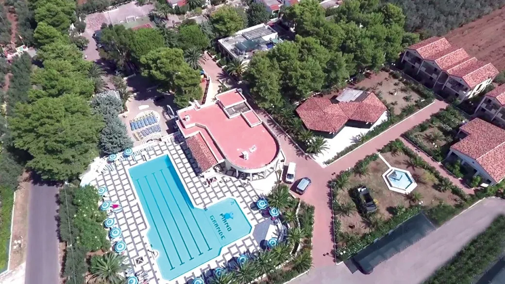 Veduta aerea del resort con piscina, edifici dai tetti rossi e giardini circondati da vegetazione