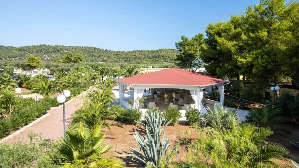 Gazebo con tetto rosso immerso nel giardino tropicale con palme e colline verdi sullo sfondo