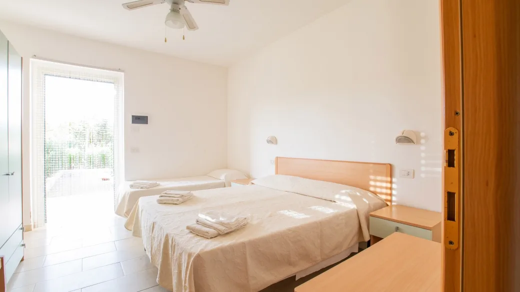 Camera tripla luminosa con letto matrimoniale e singolo, ventilatore a soffitto e ampia porta finestra