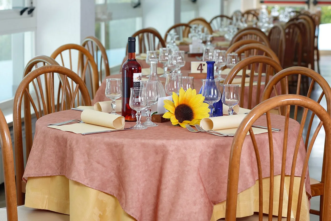 Tavolo del ristorante apparecchiato con tovaglia rosa, bicchieri e girasole decorativo