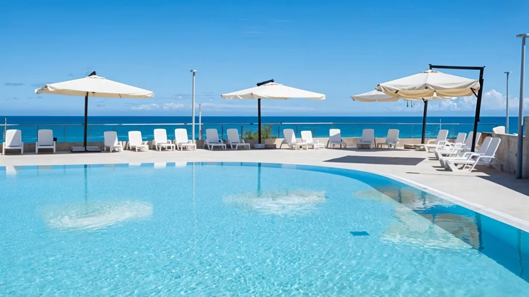 Piscina esterna con lettini bianchi, ombrelloni e vista panoramica sul mare