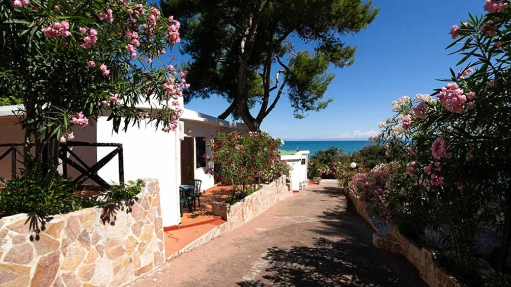 Vialetto fiorito tra bungalow bianchi con oleandri rosa e vista sul mare